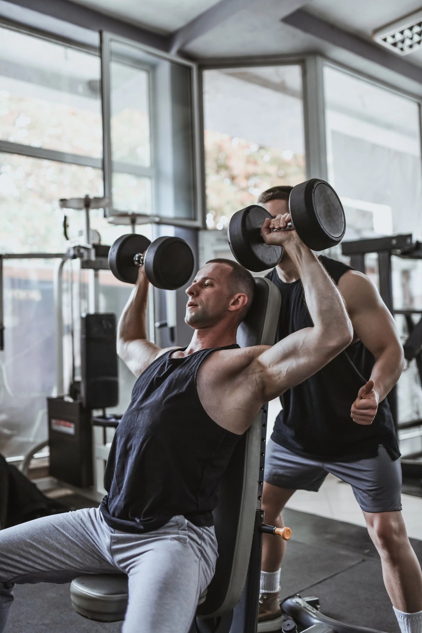 Training partners performing dumbbell shoulder press with coaching support